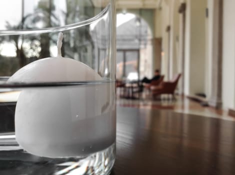 Floating candle contained in a glass vase, placed on a wooden table, in a blurred background.