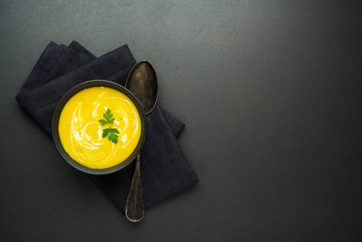 Healthy vegetable yellow cream soup on black background