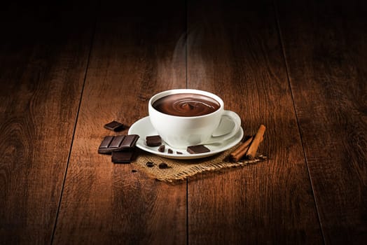 Cup of hot chocolate and cocoa with smoke on wooden background.