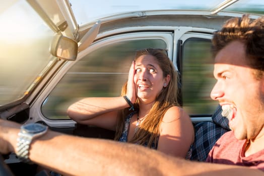 Couple in a car at sunset, with male driving fast and girl scared, screaming and praying.