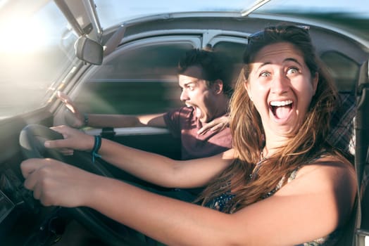 Couple in a car at sunset, with happy girl driving fast and boy scared, screaming and praying.