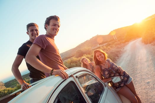 Group of happy people in a car at sunset in summer.