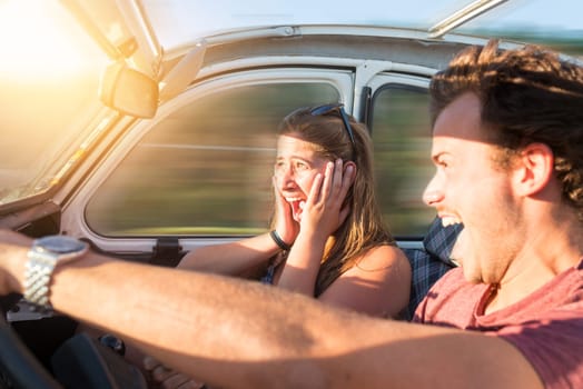 Couple in a car at sunset, with male driving fast and girl scared, screaming and praying.