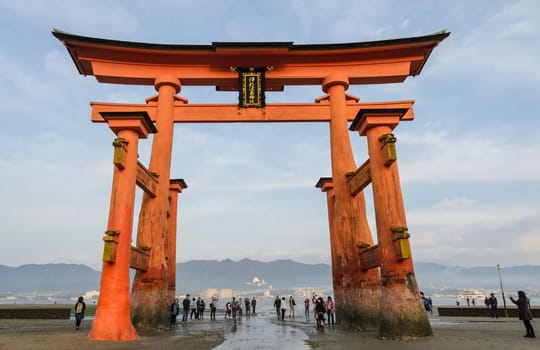 MIYAJIMA, JAPAN - NOVEMBER 20, 2016: The great O-Torii of Itsukushima Shrine. Tourists walk around the famous floating torii gate of the Itsukushima Shrine on Miyajima at low tide in Miyajima, Japan