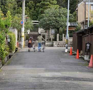 Rear view of young man and woman walking with bicycles in Kyoto, Japan