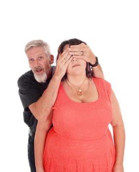 A middle age couple standing isolated for white background and the .man is holding his hands over the eyes of his wife.