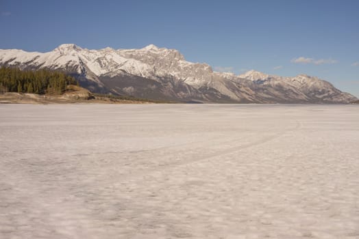Icy landscape of Abraham Lake with mountains in the background.