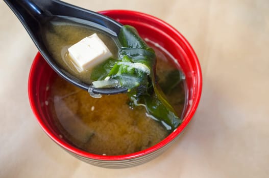 Japanese miso soup with tofu and seaweed. Clay spoonful closeup with one tofu piece