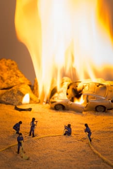 Miniature firefighters at a car accident scene in flames