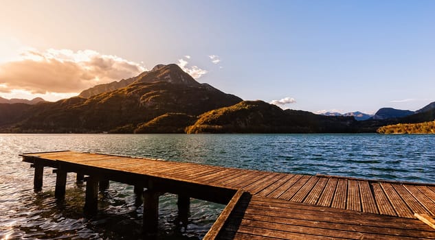 Wooden pier on the lake at sunset with mountains in the background.