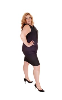 A gorgeous big blond woman standing in a black dress in profile with her.hands on her hip, isolated for white background.