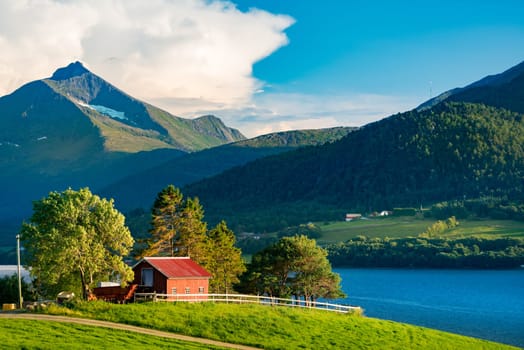 Beautiful landscape of Norway. Red barn, trees and meadows, mountains and sky in background. Travel in Scandinavia, Europe
