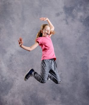 blond girl dancing and jumping in front of gray background