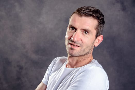 friendly young man with crossed arms in front of gray background
