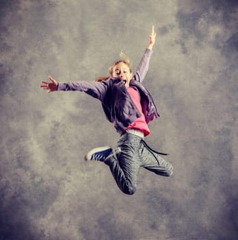 blond girl dancing and jumping in front of gray background