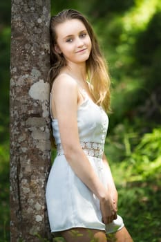 Pretty blond girl leaning against tree trunk