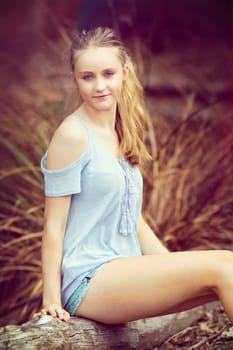 Blond teen girl sitting on log