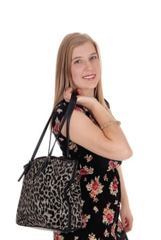 A young blond woman standing in a dress holding up her handbag,.smiling, isolated for white background.