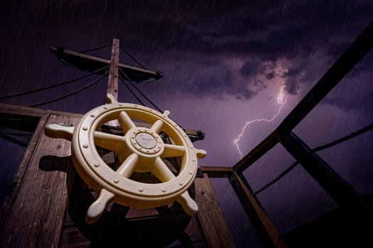 Steering wheel and wooden mast of a pirate ship during storm with stormy skies and lightening in the background