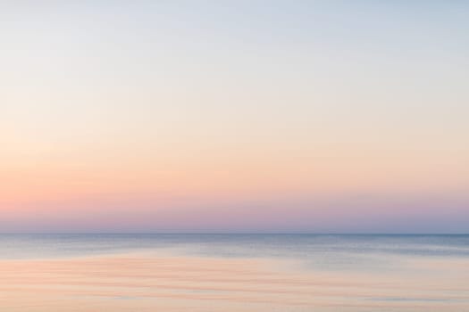 Horizontal picture of clouds in the sky above calm sea surface during sunset