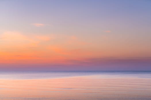 Horizontal picture of clouds in the sky above calm sea surface during sunset