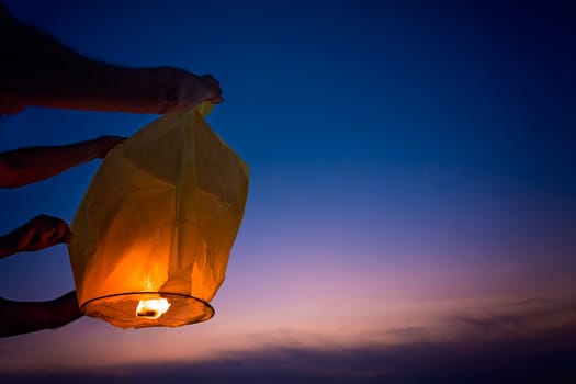 People setting off chinese lantern on the beach at sunset