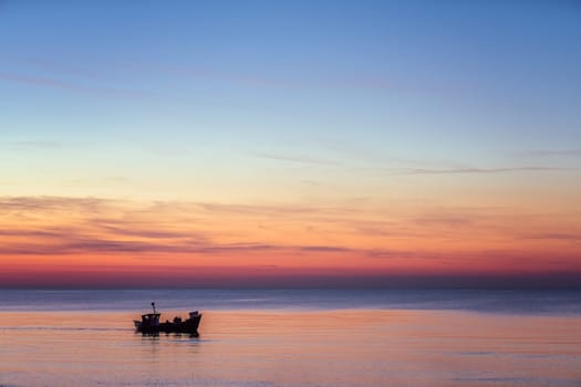 Small fisherman boat sailing at dusk on the calm sea