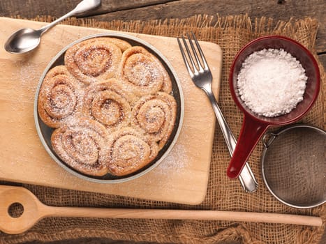 Homemade cinnamon snails with kitchen utensils on a rustic wooden kitchen table