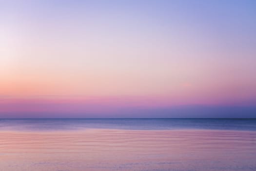 Horizontal picture of clouds in the sky above calm sea surface during sunset