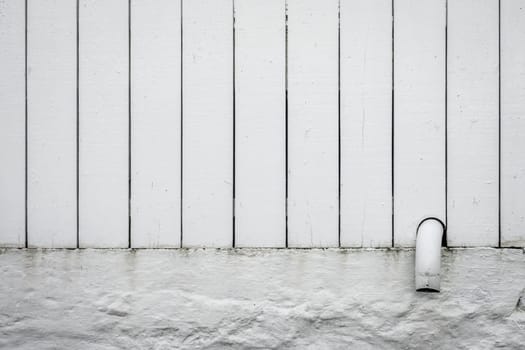 Detail of a small pipe tip sticking out of a white wooden fence