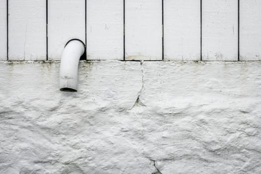 Detail of a small pipe tip sticking out of a white wooden fence