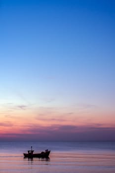 Small fisherman boat sailing at dusk on the calm sea