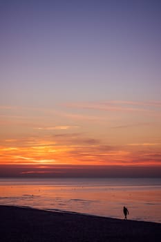 Unidentified lonely man walking on the sea beach in summer at sunset