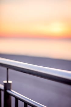 A detail of the metal iron fence of the railing on the beach promenade at sunset