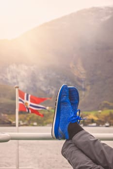 Tired tourist resting his legs on a metal barrier on a cruise ferry during Norway in a nutshell sightseeing tour through the Aurlandsfjord and Naeroyfjord fjords