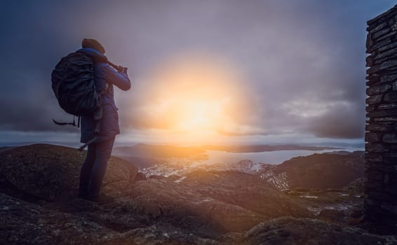 Backpacker tourist standing on the top of mount Ulriken in Bergen and taking pictures of the town and landscape below, Norway