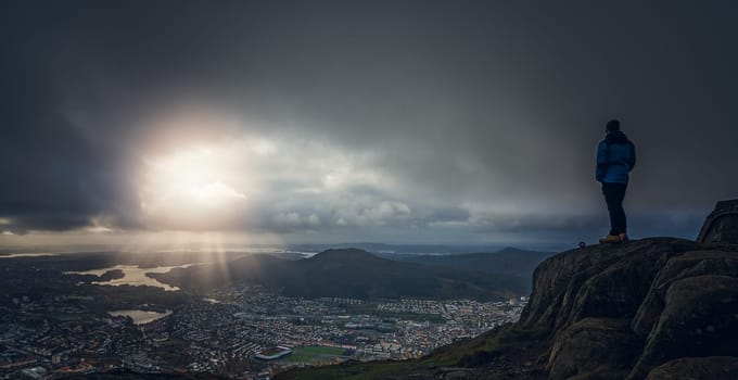 Unidentifiable tourist standing on the top of mount Ulriken in Bergen and looking at the landscape below, Norway