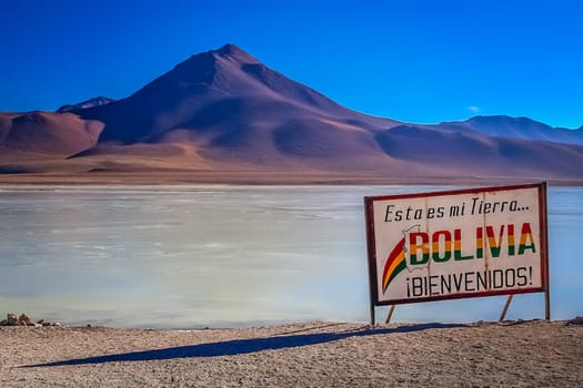 Large board marking the border between Bolivia and Chile on the shore of a salty Altiplano lagoon in the bolivian Andes