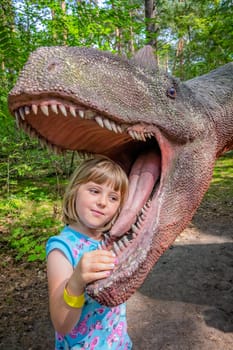 Cute little caucasian girls head in the mouth of a dinosaur replica in an amusement park