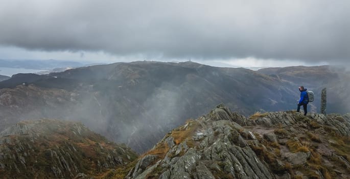 Trekker with a backpack standing on the top of mount Ulriken in Bergen and looking at the landscape below, Norway