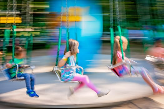 Unidentifiable children riding on a carousel in an amusement park, image with intentional movement blur