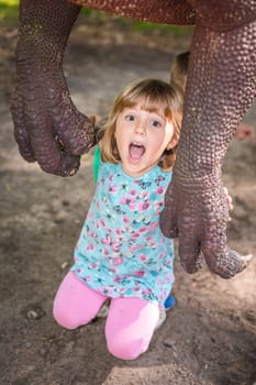 Little girls under the claws of a dinosaur replica in an amusement park