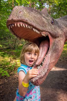 Cute little caucasian girls head in the mouth of a dinosaur replica in an amusement park