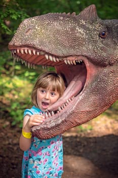 Cute little caucasian girls head in the mouth of a dinosaur replica in an amusement park