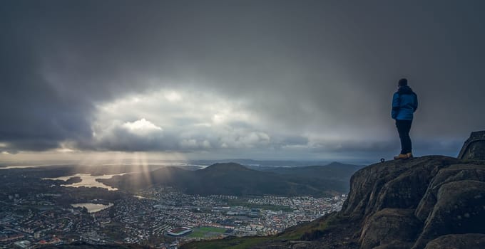 Unidentifiable tourist standing on the top of mount Ulriken in Bergen and looking at the landscape below, Norway