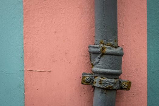 Old rusted water pipe on pink and blue wall texture background