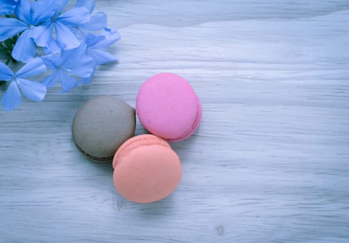 French pink macarons with blue flower on wooden background. Retro-Vintage filter effect