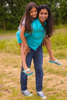 Woman carries child piggyback in summer on the meadow