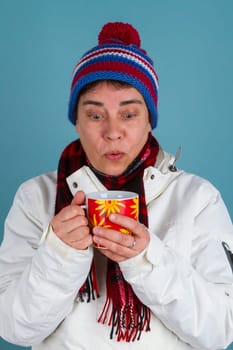 Woman drinks hot drinks in winter clothes on a blue background