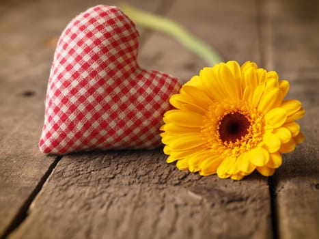Checkered heart shape with a yellow gerbera daisy on a rustic wooden table, Valentines Day background